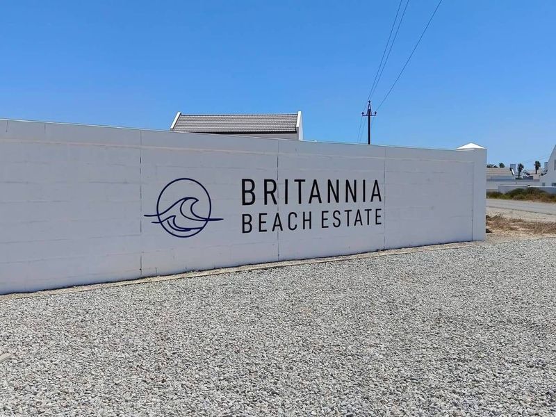 Entrance view of Britannia Beach Estate featuring a clean white boundary wall with estate branding and a gravel approach.