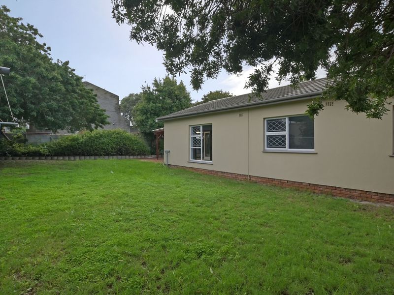 Rear view of the house featuring a lawn, brick plinth foundation, tiled roof, and windows with security bars.