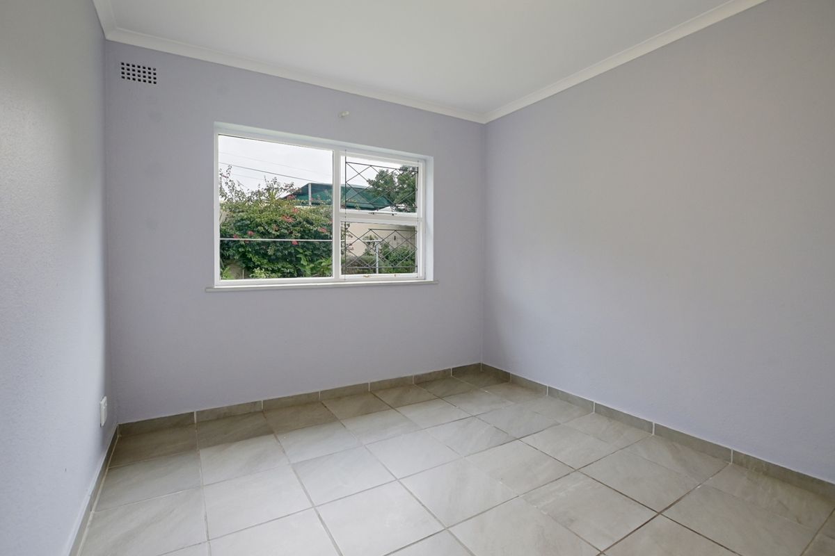 A clean, empty bedroom featuring neutral wall paint, tiled flooring, and a window with security bars.
