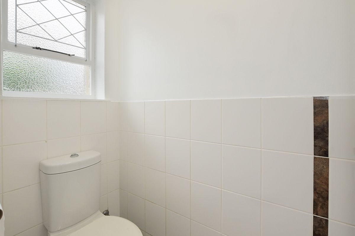 A clean, functional bathroom featuring white wall tiles with a decorative accent strip and a leaded glass window.