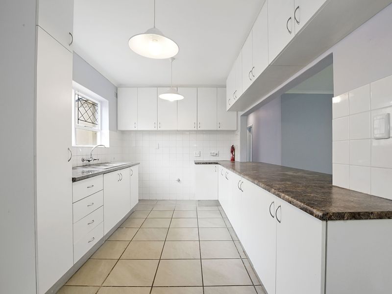 A clean, functional kitchen featuring white cabinetry, laminate countertops, tiled flooring, and a convenient pass-through window to the adjacent living area.