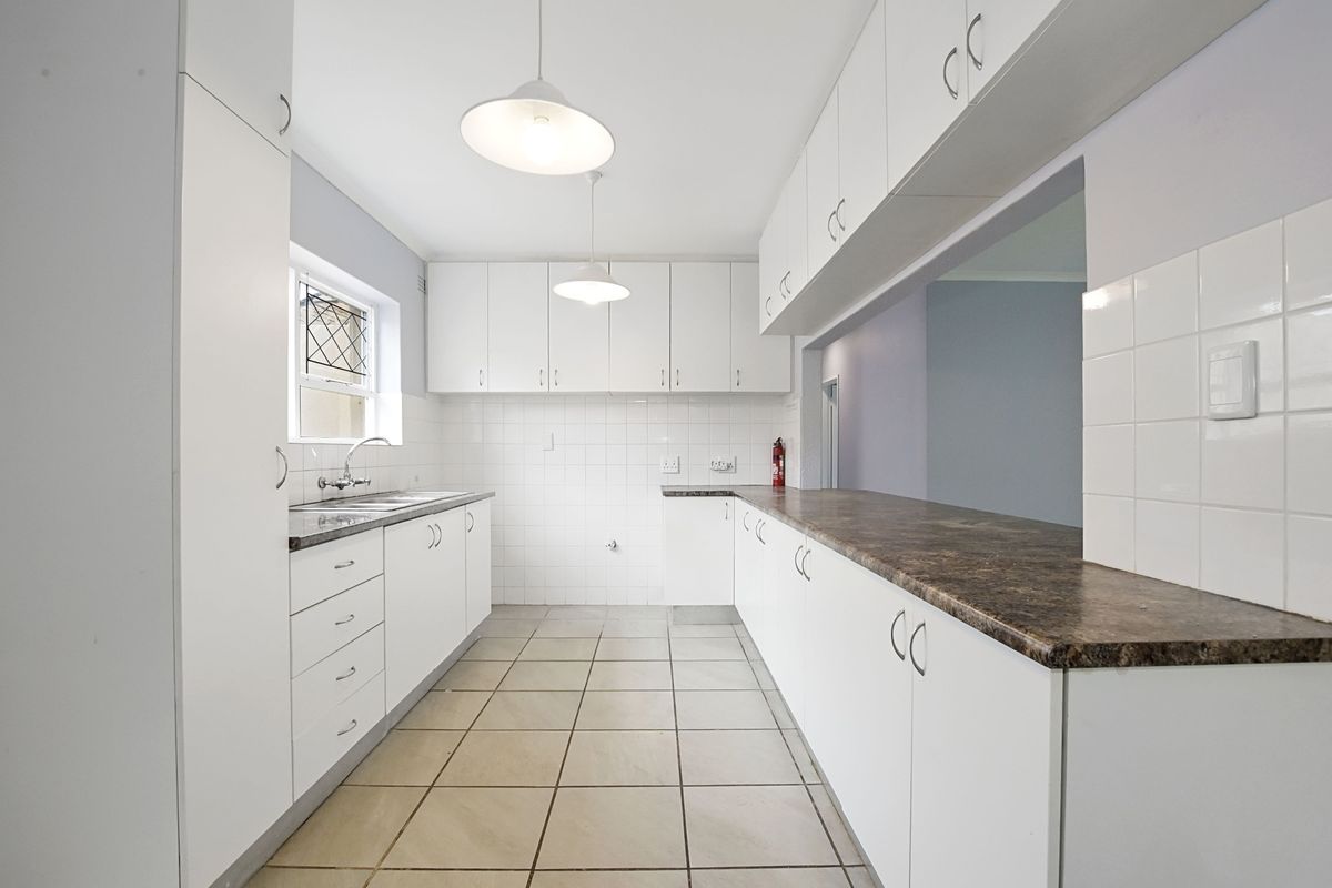 A clean, functional kitchen featuring white cabinetry, laminate countertops, tiled flooring, and a convenient pass-through window to the adjacent living area.