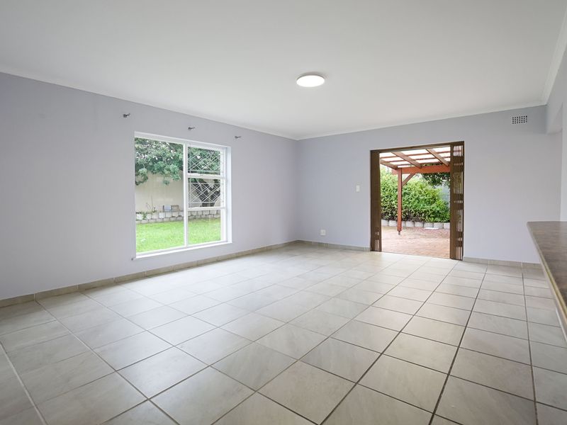 Spacious open-plan living area featuring neutral tiled flooring, a breakfast counter, and direct access to an outdoor patio area.