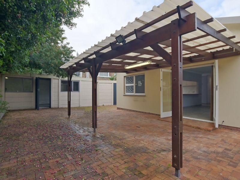 A covered outdoor patio area featuring a timber pergola structure and brick paving, providing direct access to the interior living space.