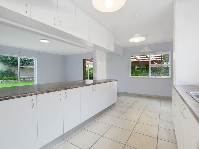 A bright and spacious kitchen featuring white cabinetry, laminate countertops, ceramic tiled flooring, and large windows overlooking the garden.