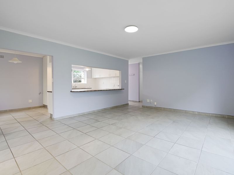 An open-plan living and dining area featuring neutral tiled flooring, coved cornicing, and a convenient pass-through window connecting to the kitchen.