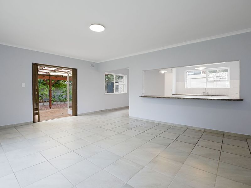 Spacious open-plan living area featuring neutral tiled flooring, a breakfast bar overlooking the kitchen, and direct access to an outdoor patio area.