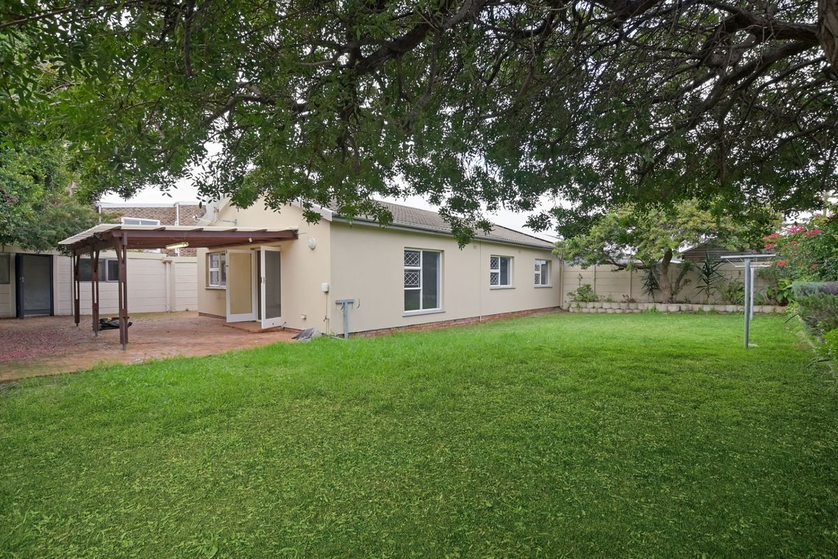 Rear view of the property featuring a spacious lawn, a covered patio area with a timber pergola, and established boundary walls.