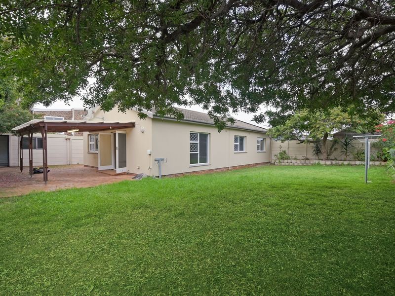 Rear view of the property featuring a spacious lawn, a covered patio area with a timber pergola, and established boundary walls.