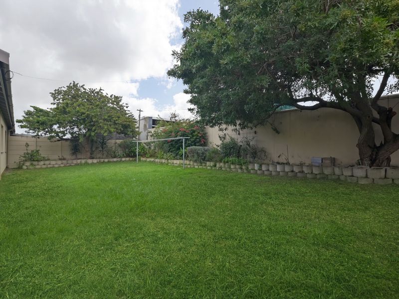 A spacious private backyard featuring a well-maintained lawn, mature trees, and perimeter boundary walls.