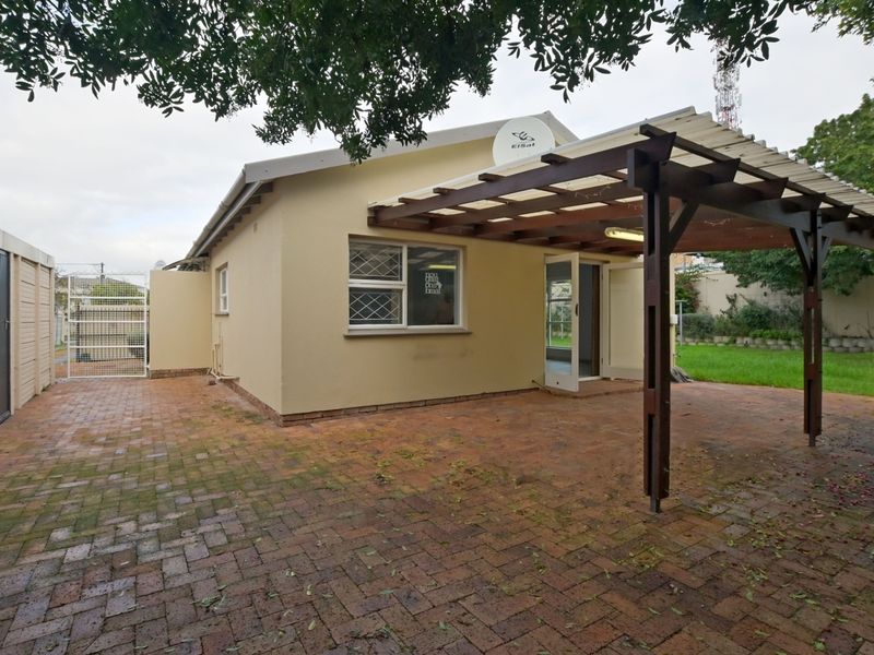 Rear exterior view featuring a brick-paved patio area with a timber pergola, security features, and access to the garden.