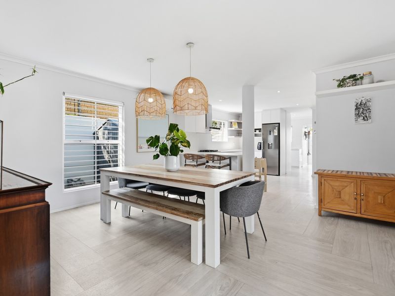 Bright open-plan living and dining area featuring wood-look tile flooring, modern kitchen with island, and neutral finishes throughout.