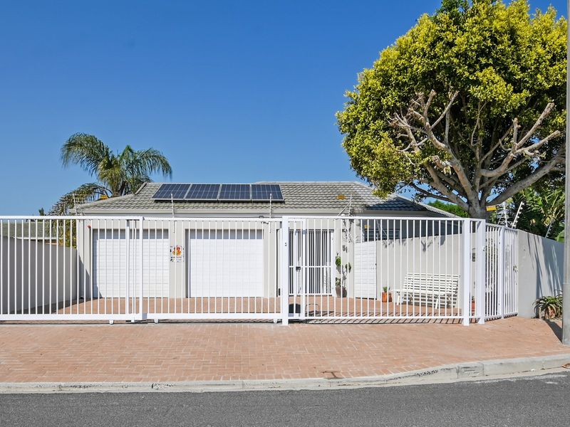 Front elevation of a well-maintained house featuring a paved driveway, double garage, security fencing, and roof-mounted solar panels.