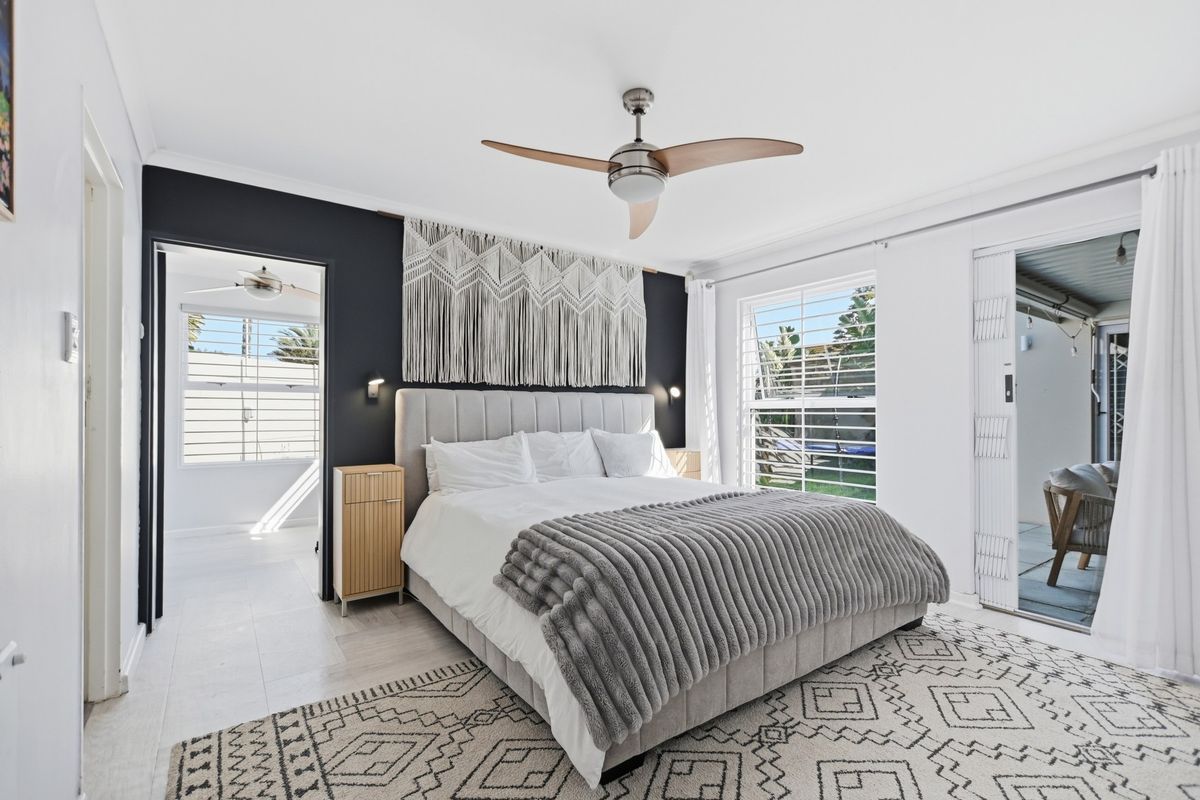 A well-maintained bedroom featuring tiled flooring, a modern ceiling fan, plantation shutters, and direct access to an outdoor patio area.