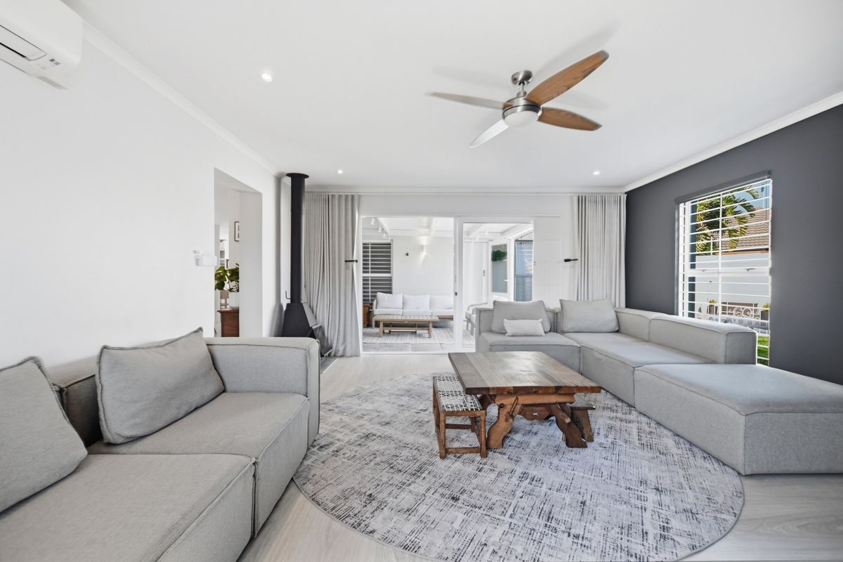 Spacious living room featuring a modern freestanding fireplace, ceiling fan, split-system air conditioning, and seamless access to the outdoor patio area.
