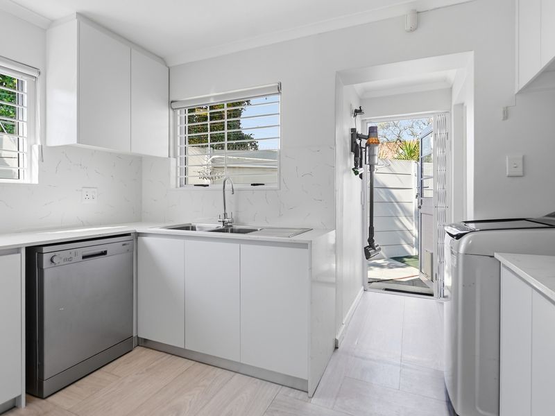 A clean and functional laundry room featuring modern white cabinetry, marble-look splashbacks, a stainless steel sink, and direct access to the exterior.
