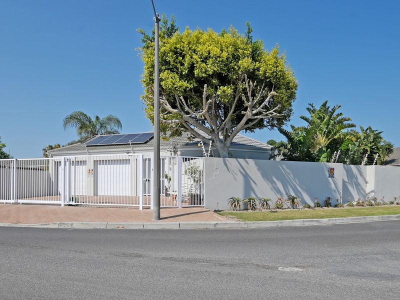 Front view of a residential property featuring a paved driveway, double garage, secure perimeter wall with electric fencing, and installed solar panels.