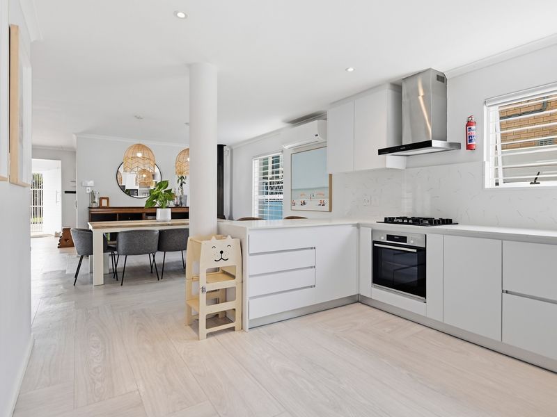 Modern open-plan kitchen and dining area featuring sleek white cabinetry, stone benchtops, integrated appliances, and light-toned flooring throughout.