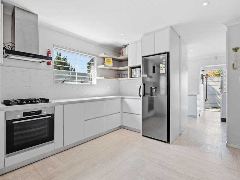 Modern kitchen featuring white cabinetry, marble-look splashback, gas cooktop, built-in oven, and integrated storage with light wood-look flooring.