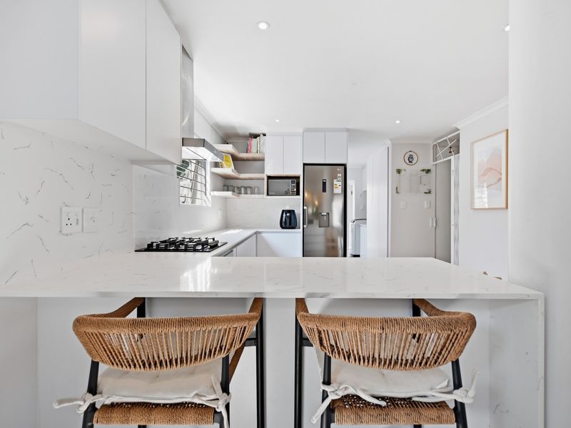 Modern kitchen featuring white cabinetry, marble-look quartz countertops, a gas cooktop, and a functional breakfast bar with integrated lighting.