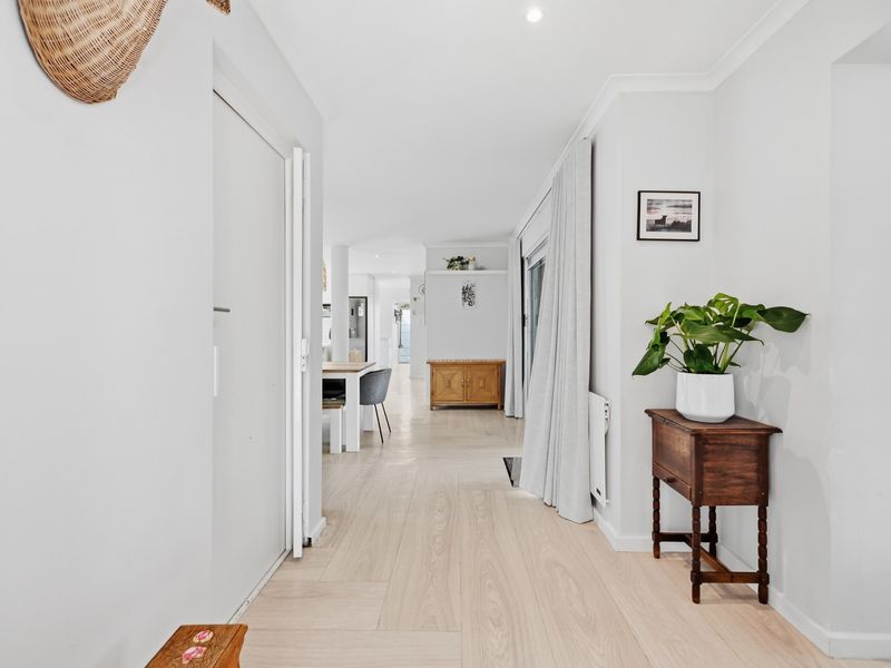 A bright and well-maintained hallway featuring light-toned laminate flooring, recessed downlighting, and a seamless transition into the open-plan living area.
