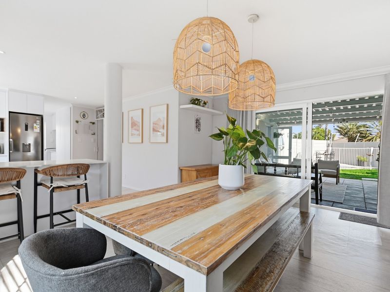Bright open-plan living and dining area featuring a modern kitchen island, tiled floors, and seamless access to the outdoor patio through sliding glass doors.