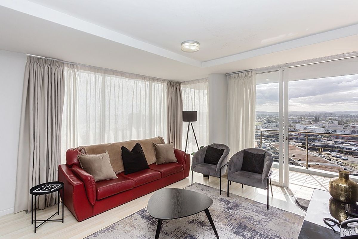 Bright living room featuring large floor-to-ceiling windows, tiled flooring, and direct access to a balcony with expansive city views.