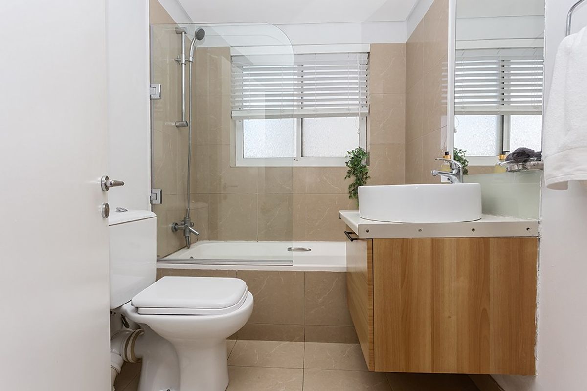 A well-maintained bathroom featuring a built-in vanity with a vessel sink, a bathtub with a glass shower screen, and neutral wall tiling.