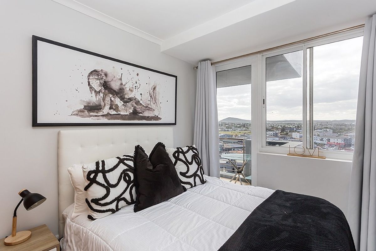 A well-maintained bedroom featuring a large window and sliding glass door that provides access to a balcony with expansive city views.