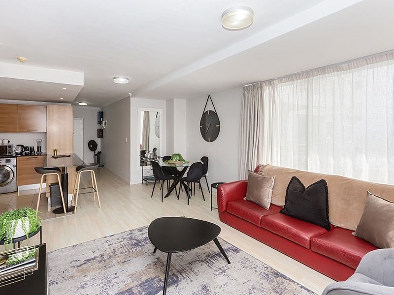 Open-plan living area featuring a modern kitchen with built-in cabinetry, integrated laundry appliances, and a breakfast bar, flowing into a bright lounge space.