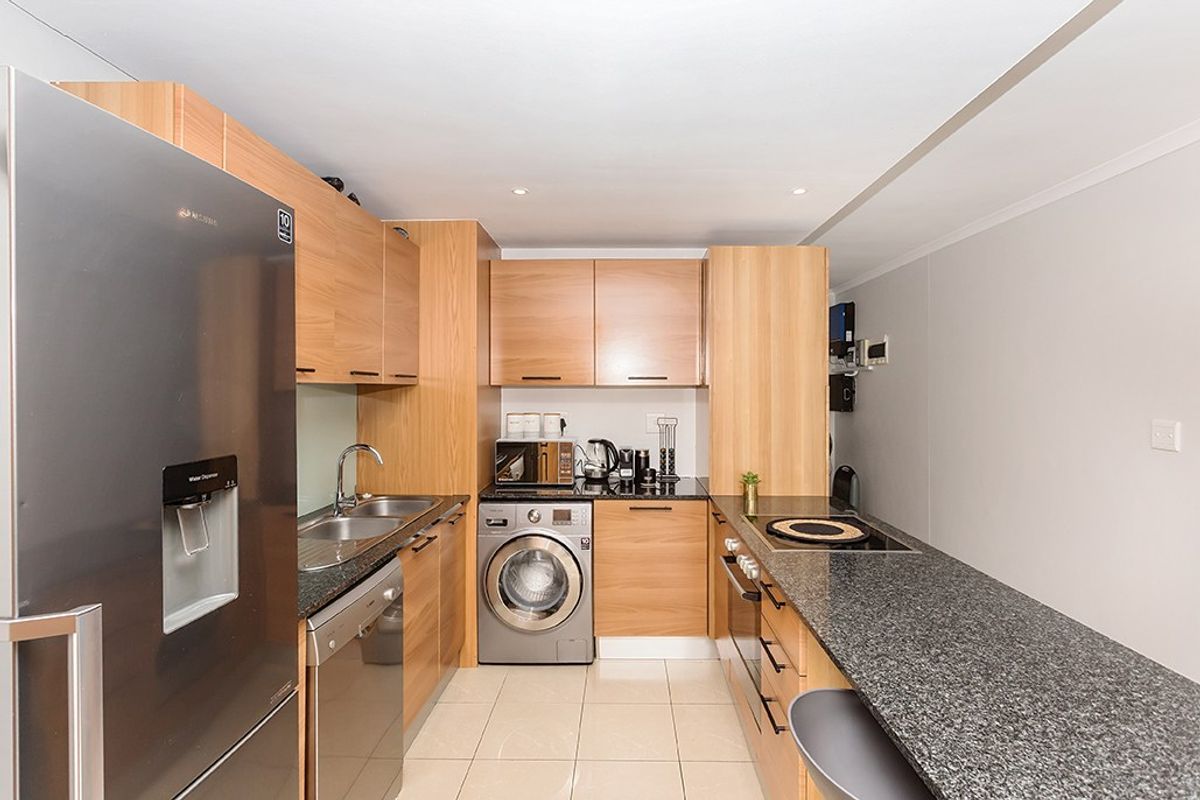 Modern kitchen featuring light wood cabinetry, granite countertops, integrated appliances, and tiled flooring with a breakfast bar area.