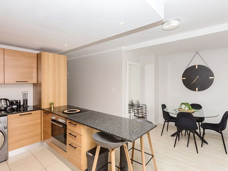 Modern open-plan kitchen and dining area featuring light wood cabinetry, granite countertops, integrated appliances, and neutral tiled flooring.