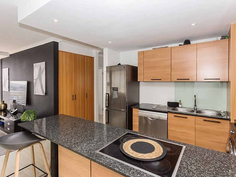 Modern open-plan kitchen featuring granite countertops, wood-finish cabinetry, integrated electric cooktop, and recessed lighting, seamlessly flowing into the living area.