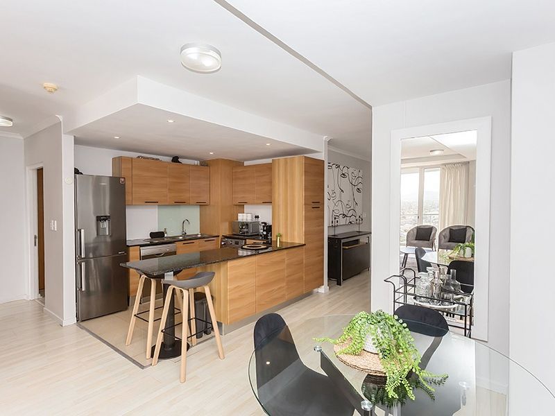 Modern open-plan kitchen featuring light wood cabinetry, granite countertops, and integrated appliances, seamlessly flowing into the dining and living areas.