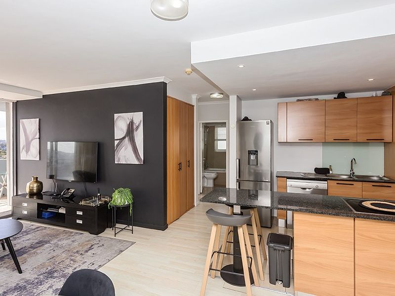 Modern open-plan living area featuring a well-appointed kitchen with granite countertops, wood-finish cabinetry, and seamless flow to the lounge and balcony.