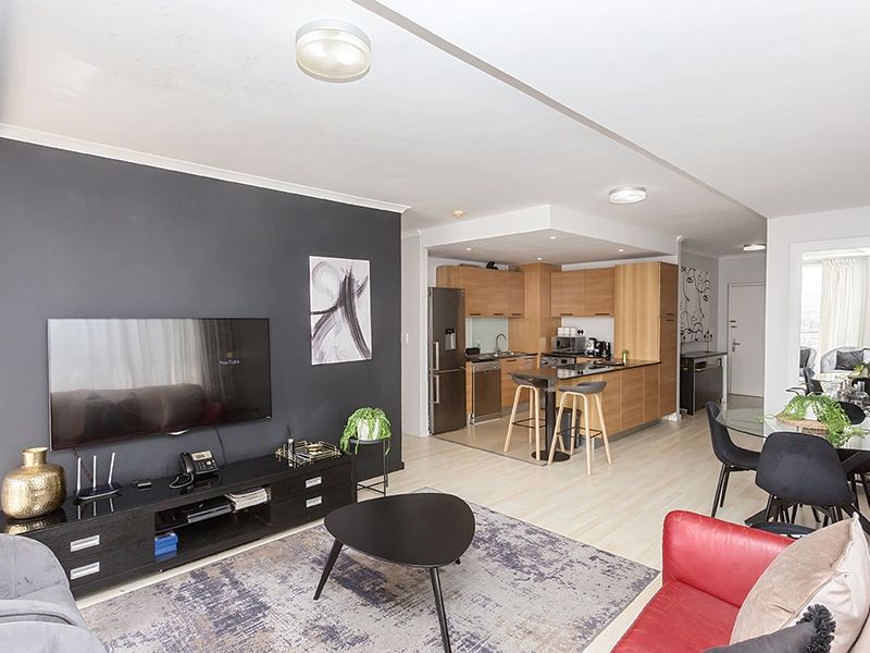 Open-plan living area featuring a modern kitchen with wood-finish cabinetry, a central island, and light laminate flooring throughout the combined space.