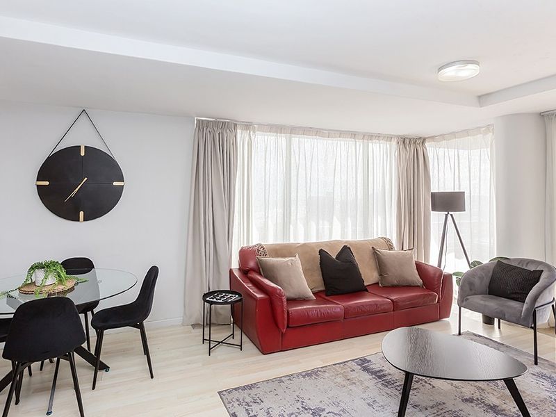 A bright and open living area featuring light-toned laminate flooring, neutral walls, and large windows dressed with floor-to-ceiling curtains.