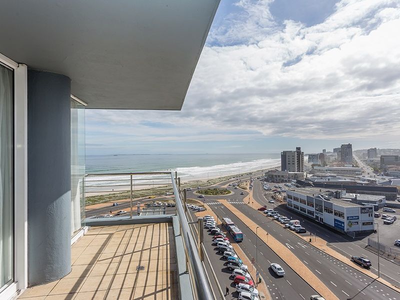 A spacious balcony featuring tiled flooring and a stainless steel balustrade, offering expansive coastal and urban views.