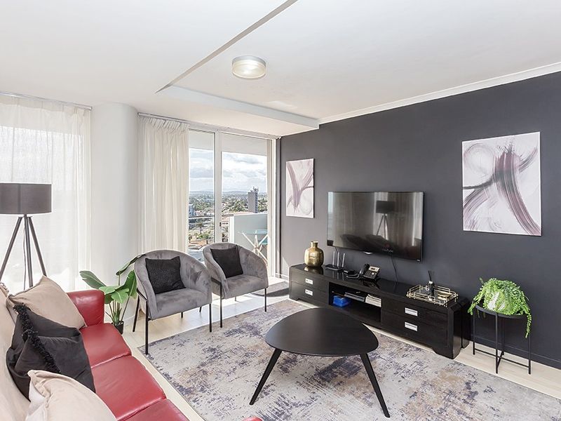 A modern living room featuring dark accent walls, laminate flooring, and large sliding glass doors that provide natural light and access to the balcony.