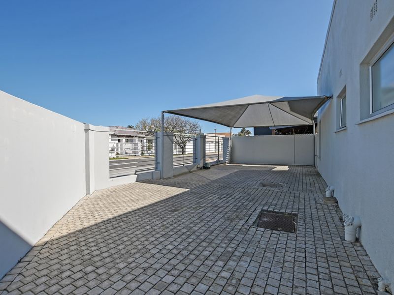 A paved front driveway area featuring a shade sail, secure boundary wall, and metal gate access.
