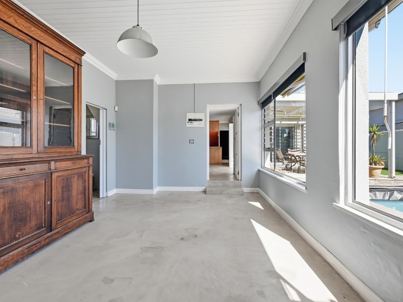 A bright, open living area featuring polished concrete floors, tongue and groove ceilings, and large windows overlooking the pool area.