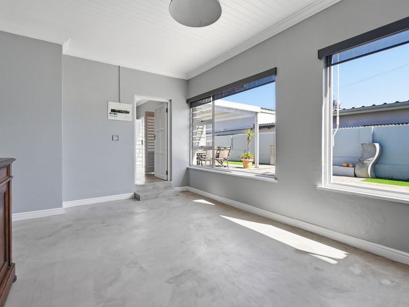 A bright, empty living area featuring polished concrete floors, tongue and groove ceilings, and large windows providing natural light and views of the rear patio.