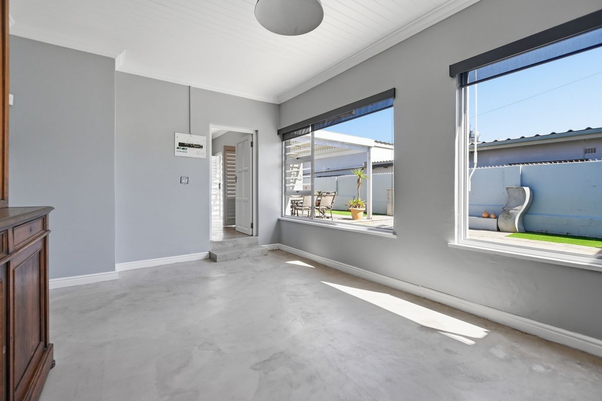 A bright, empty living area featuring polished concrete floors, tongue and groove ceilings, and large windows providing natural light and views of the rear patio.