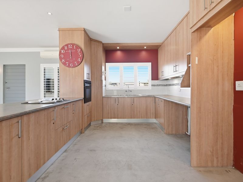 Spacious kitchen featuring light wood-look cabinetry, built-in oven, cooktop, and concrete flooring, offering a functional layout with ample storage and preparation space.
