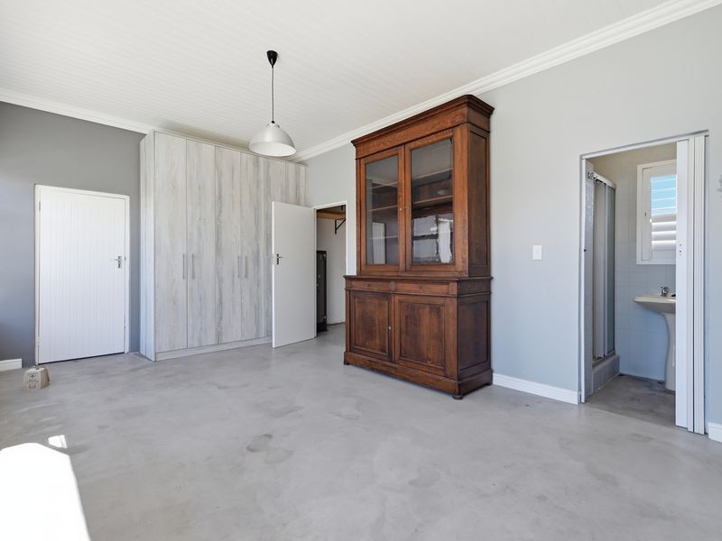 A bedroom featuring concrete flooring, built-in cupboards, and direct access to an en-suite bathroom with a pedestal basin and shower.