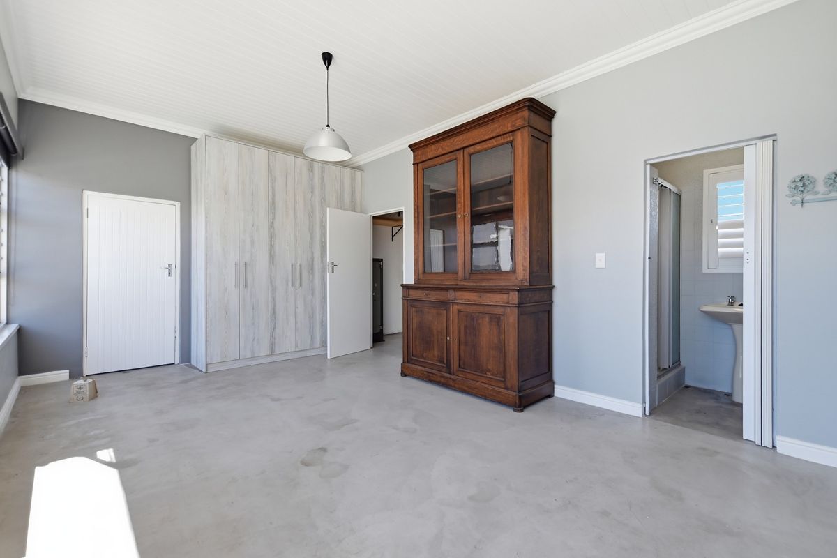 A bedroom featuring concrete flooring, built-in cupboards, and direct access to an en-suite bathroom with a pedestal basin and shower.