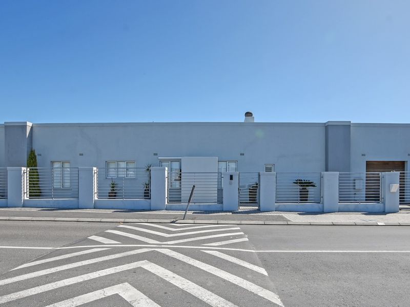 Front elevation of a modern single-story house featuring a secure perimeter fence, gated entrance, and paved driveway access from the street.