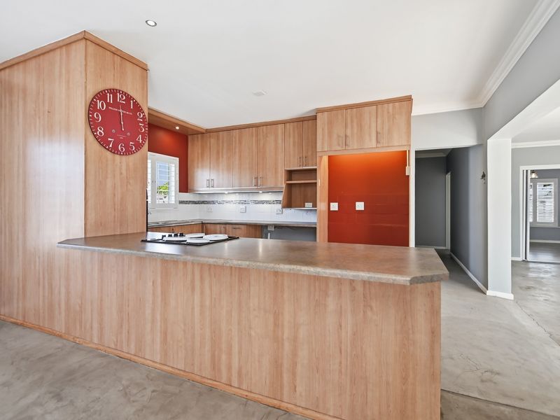 A functional kitchen featuring wood-look cabinetry, a breakfast bar with an integrated hob, and a tiled backsplash, offering a clean and open layout.