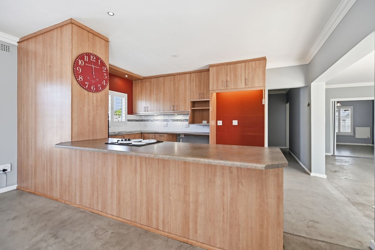 A functional kitchen featuring wood-look cabinetry, a breakfast bar with an integrated hob, and a tiled backsplash, offering a clean and open layout.