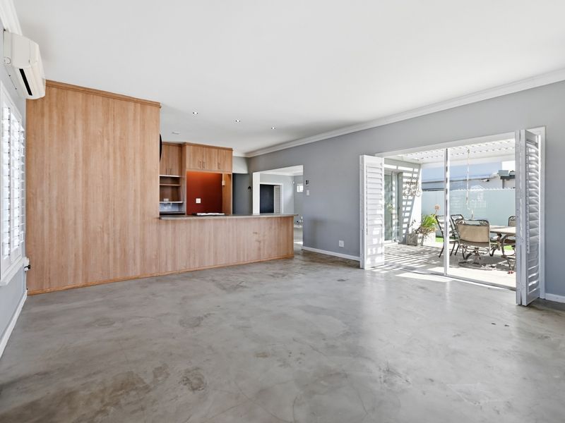 Spacious open-plan living area featuring polished concrete floors, built-in kitchen cabinetry with a breakfast bar, and direct access to an outdoor patio through sliding doors.
